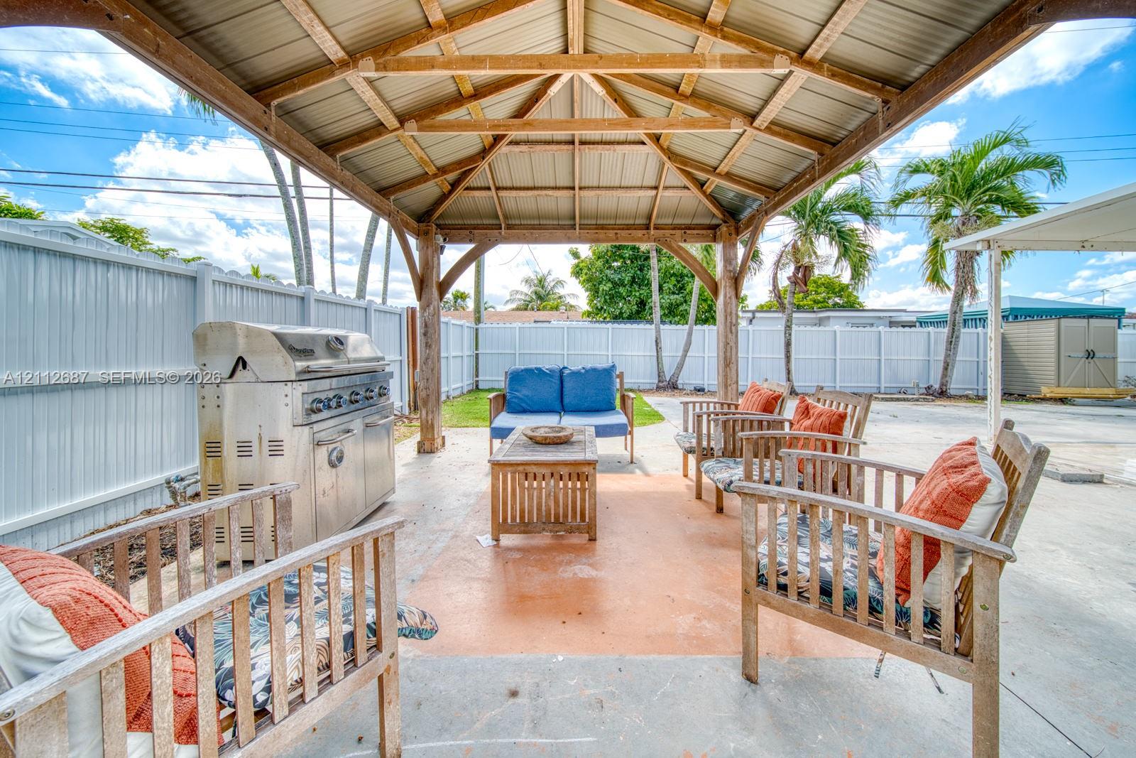 Covered outdoor pavilion featuring heavy timber framing, a metal roof, concrete patio, and built-in stainless steel grill