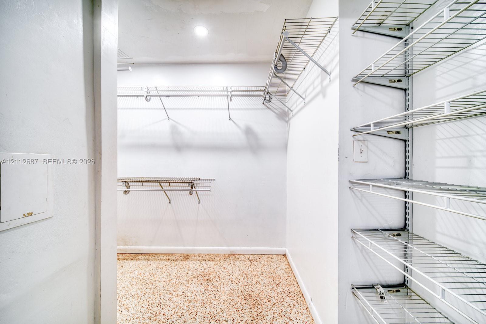 Walk-in storage space featuring multi-tiered white wire shelving systems and speckled composite flooring