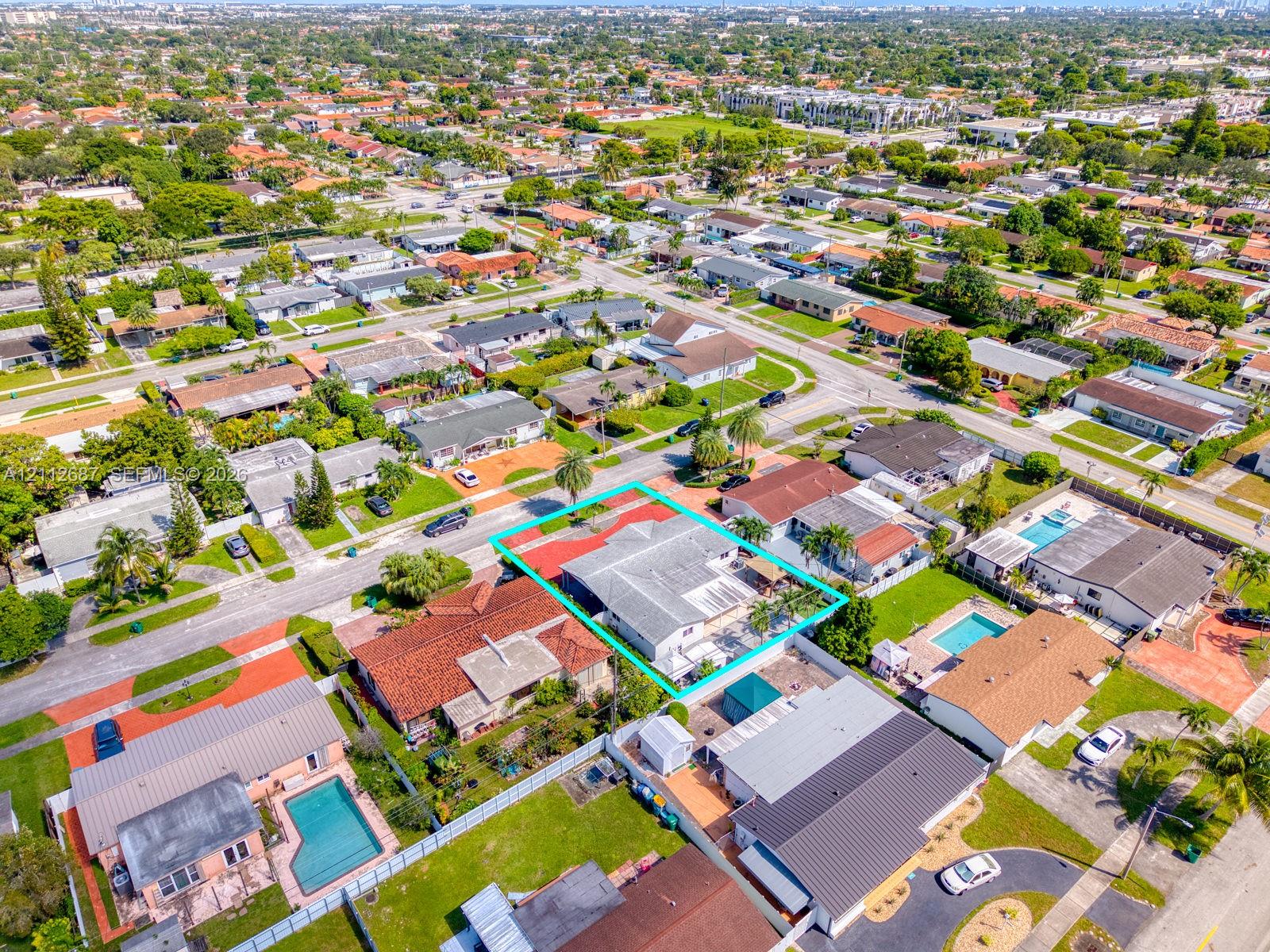 Aerial perspective featuring a single-story residence with a multi-hipped roof, paved driveway, enclosed backyard, and mature landscaping