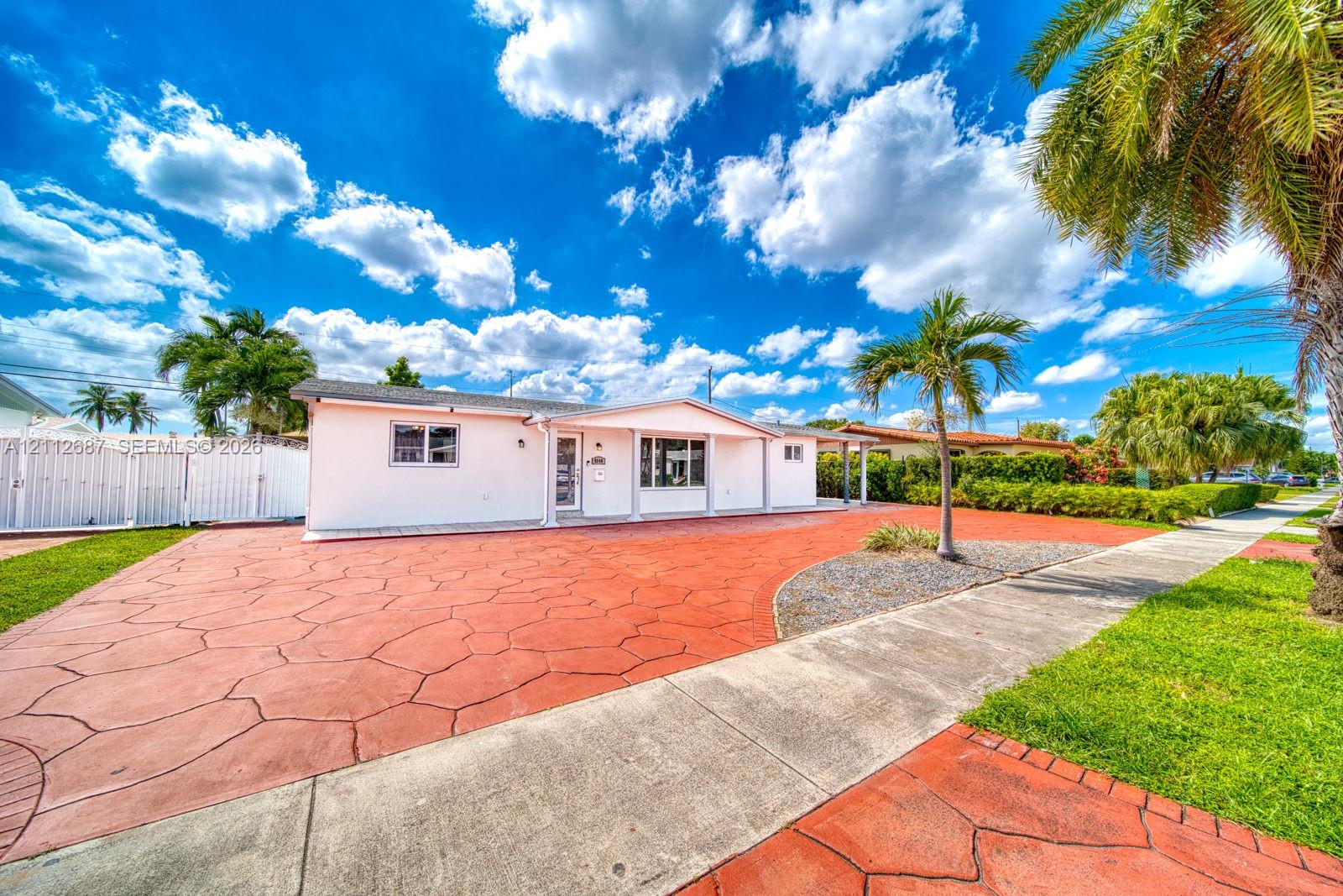 Single-story exterior featuring white stucco siding, expansive stamped concrete driveway, and mature landscaping