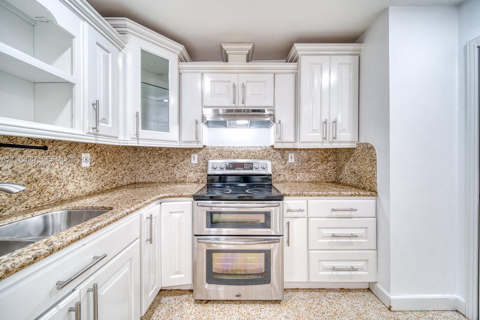 Kitchen featuring white shaker-style cabinetry, stone-finish countertops with matching backsplash, stainless steel double-oven range, and an undermount sink