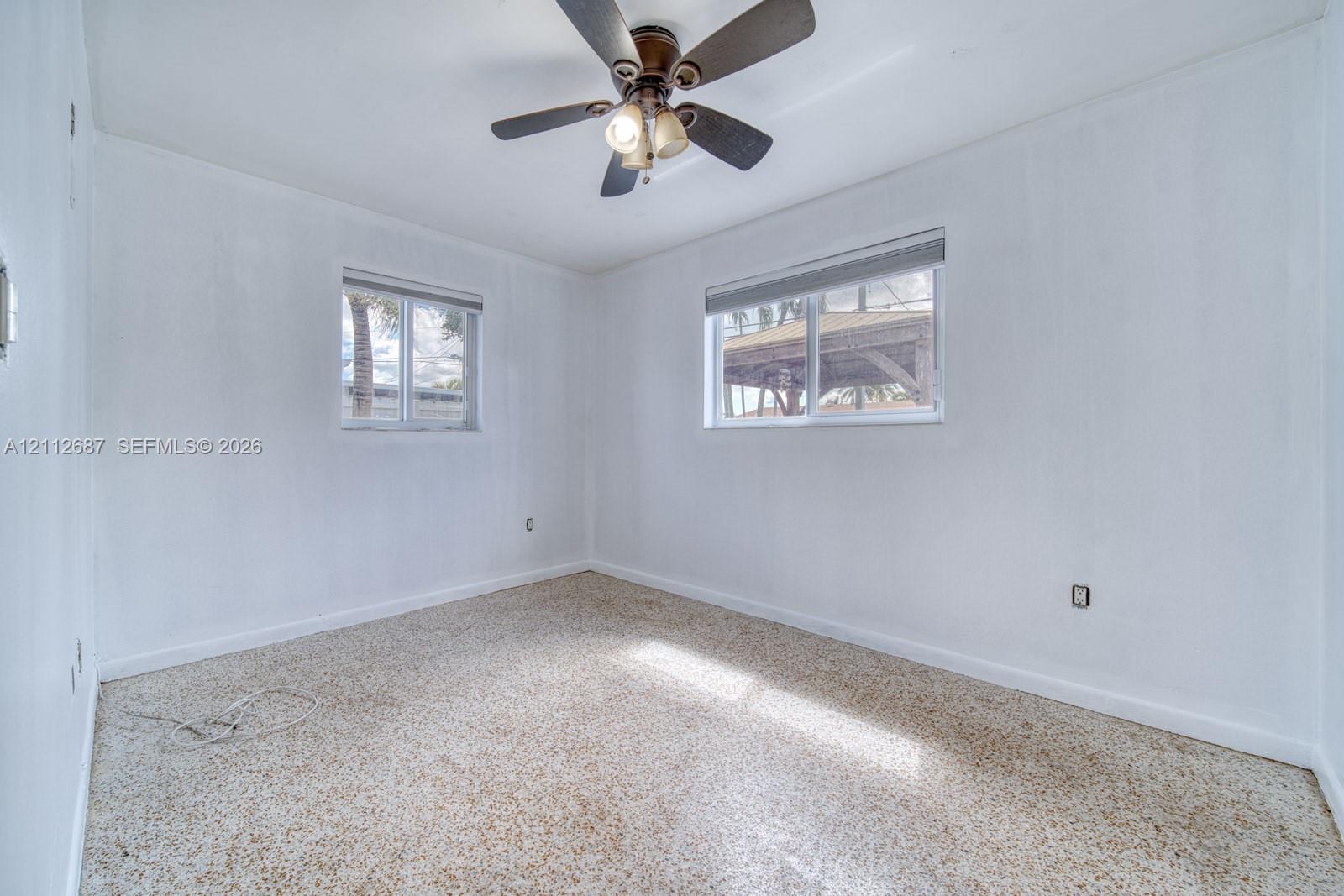 Neutral-toned interior featuring terrazzo flooring, two sliding-sash windows with roller shades, and a ceiling fan with integrated lighting