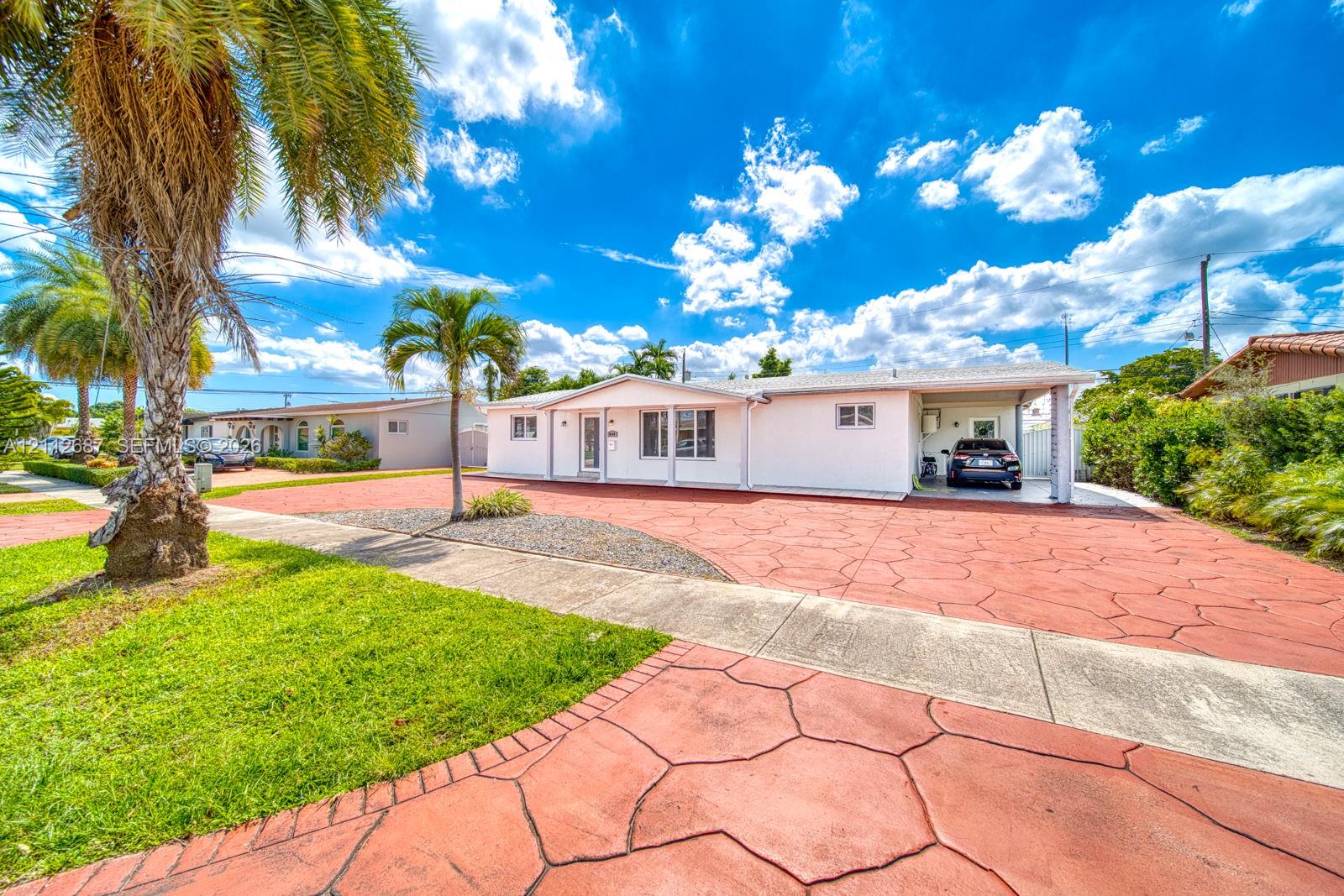 Single-story exterior featuring white stucco siding, a covered carport, and extensive stamped concrete driveway