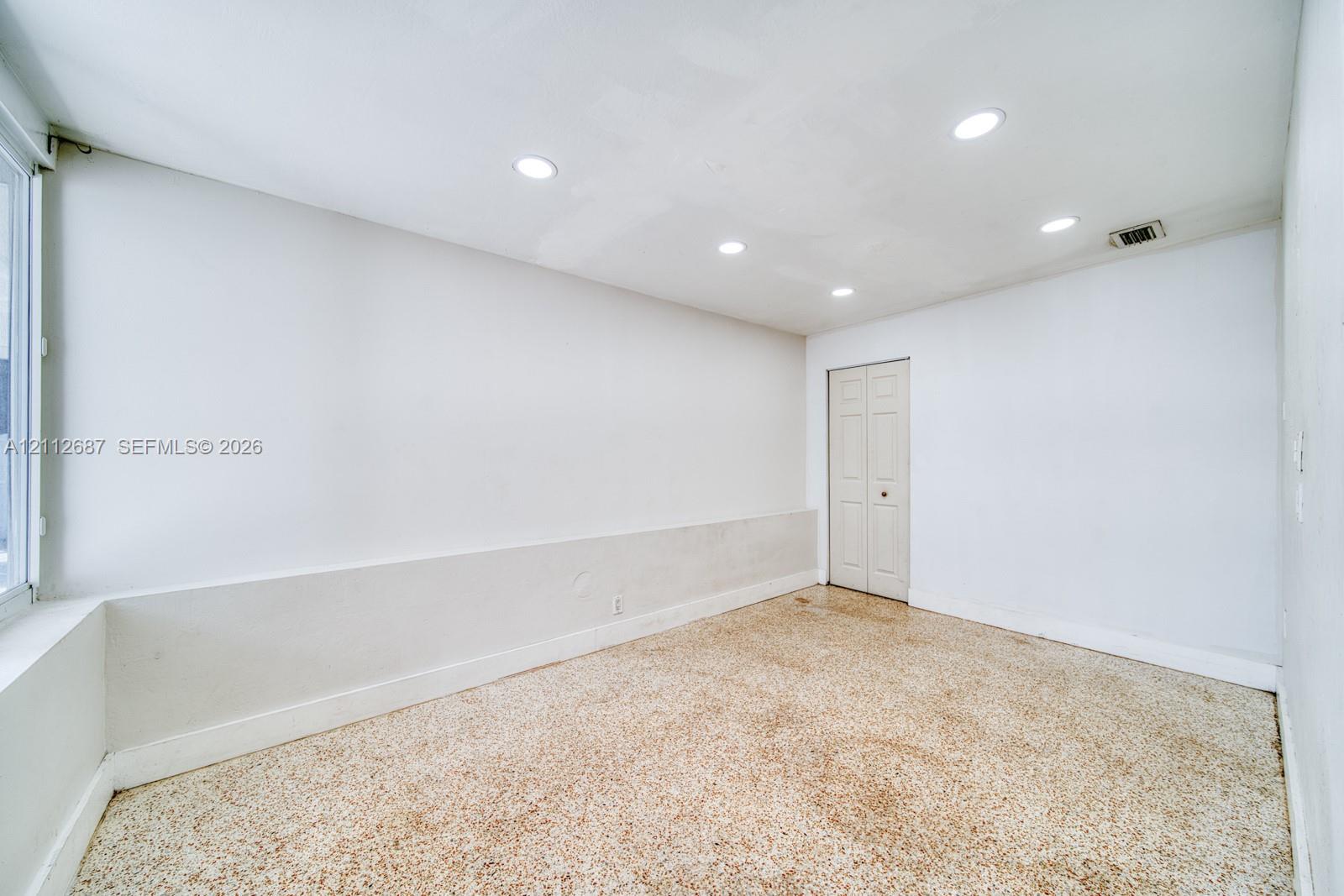 Neutral-toned room featuring recessed ceiling lighting, a bi-fold closet door, and patterned resilient flooring