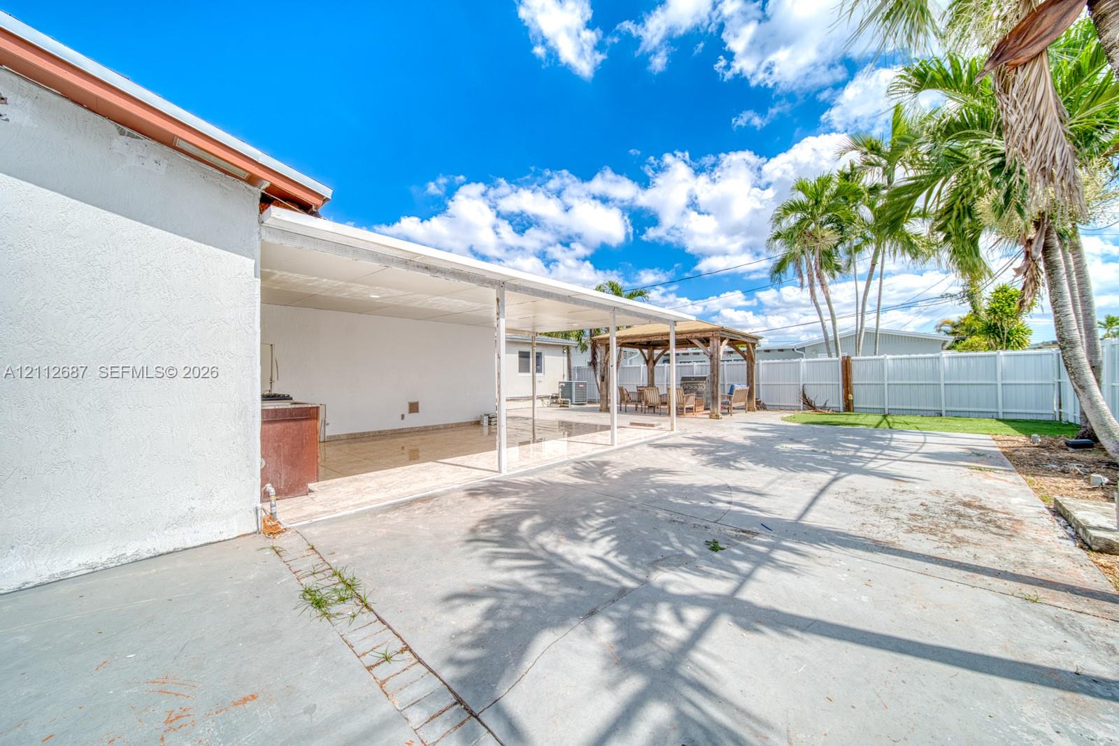 Expansive concrete patio featuring a covered lanai, built-in outdoor kitchen station, freestanding gazebo, and full perimeter privacy fencing