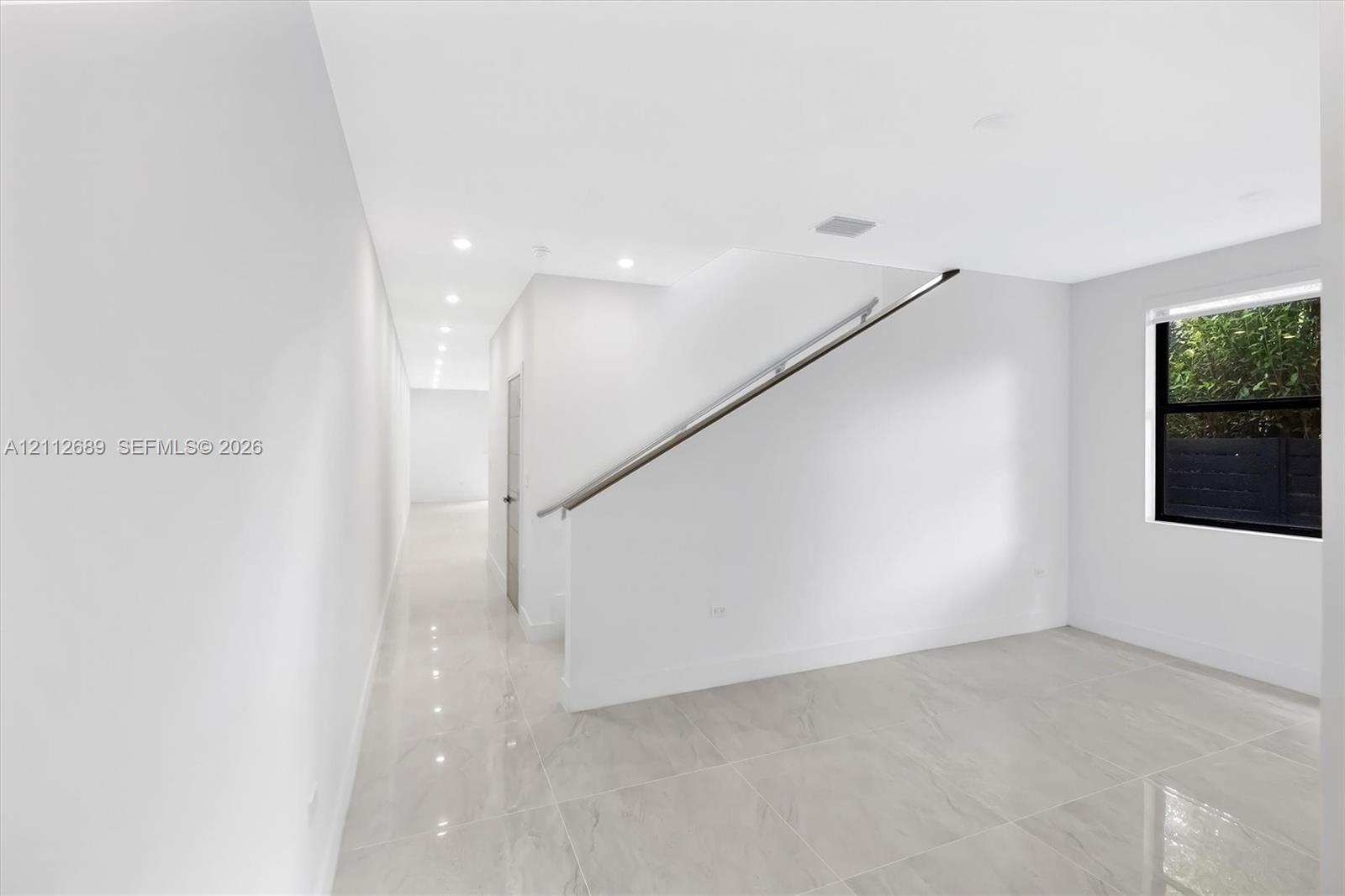 Neutral interior space featuring polished tile flooring, recessed ceiling lighting, and a staircase with a minimalist metal handrail