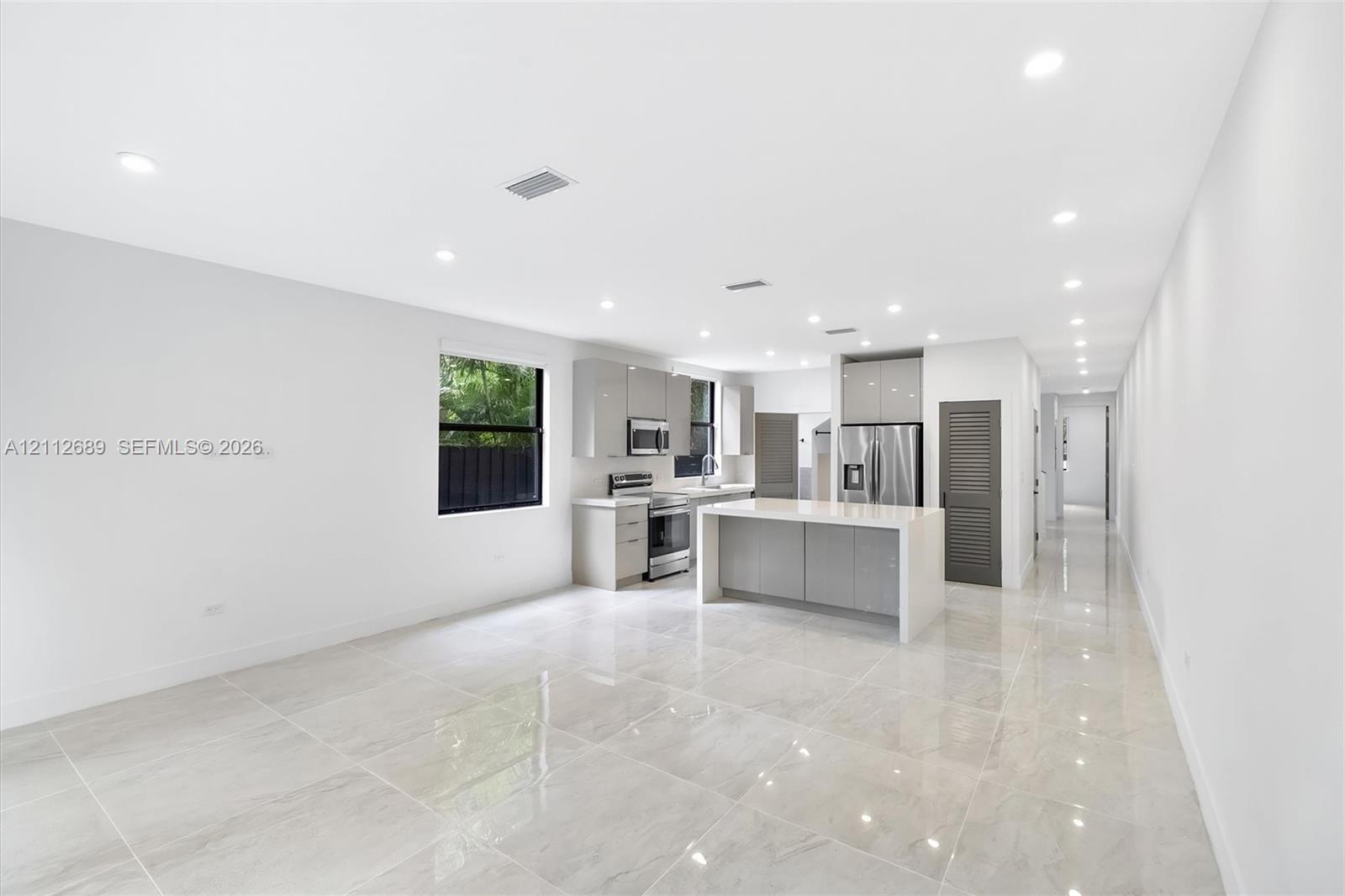 Kitchen featuring high-gloss cabinetry, stone-finish countertops, stainless steel appliances, a central island, and large-format porcelain tile flooring