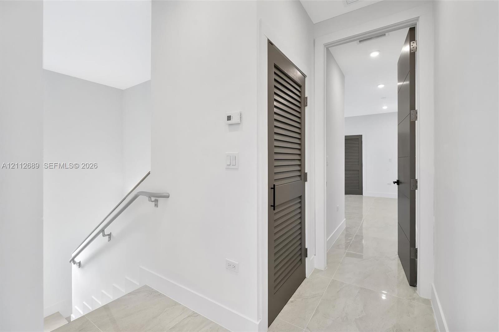 Neutral-toned tile flooring, louvered-style closet door, solid-core interior doors with matte black hardware, and recessed ceiling lighting