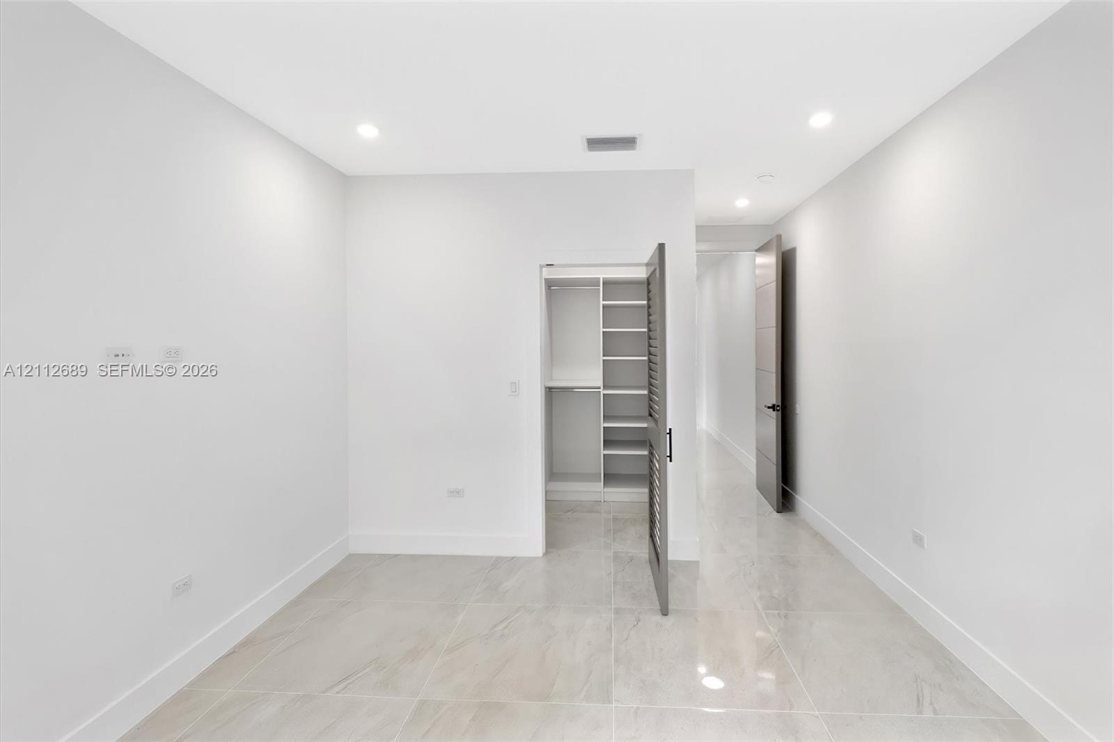 Neutral-toned porcelain tile flooring, recessed ceiling lighting, and a walk-in closet featuring built-in shelving