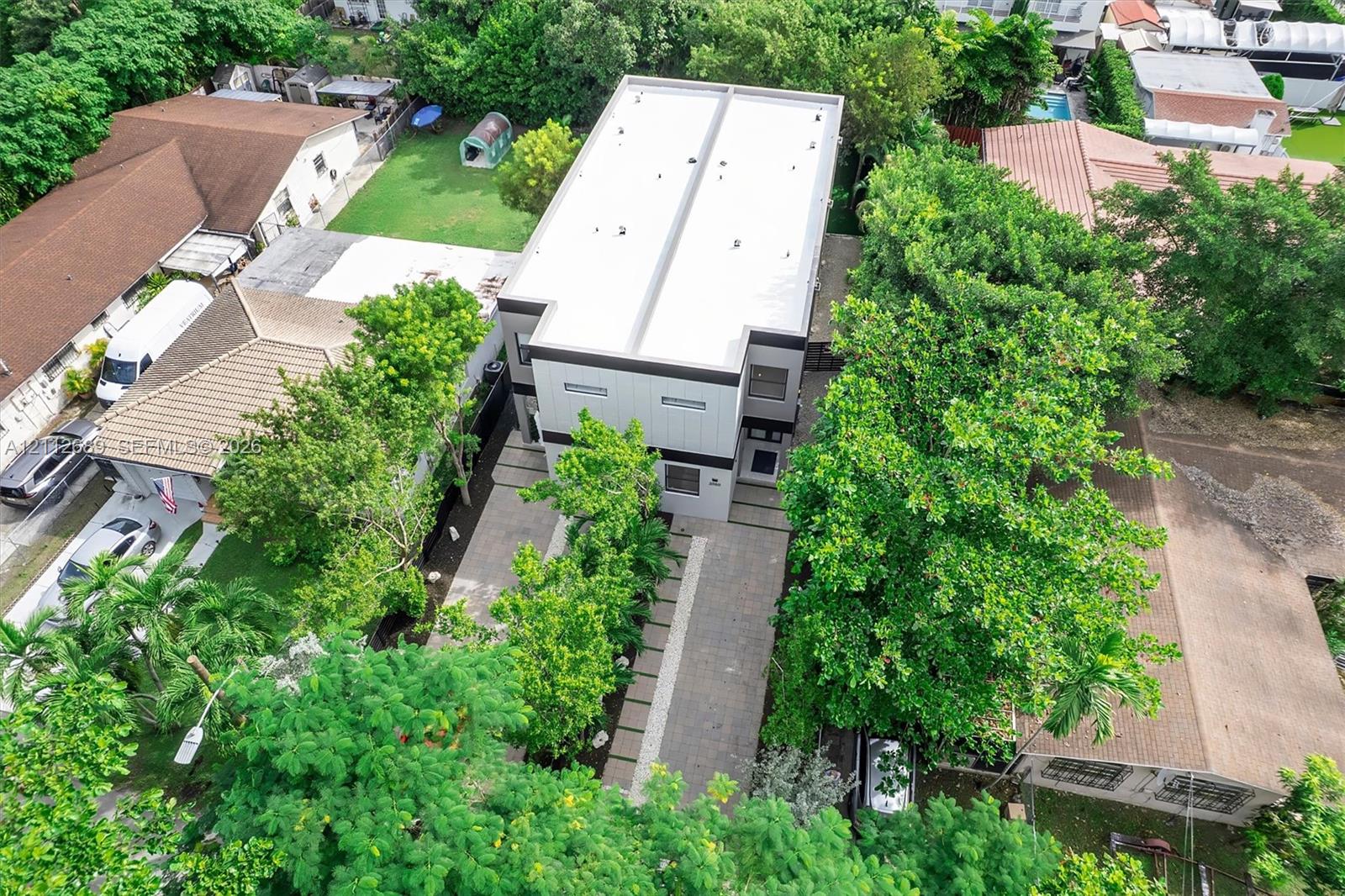 Two-story modern exterior featuring a flat roof, paver driveway, linear concrete pavers, and surrounding mature landscaping