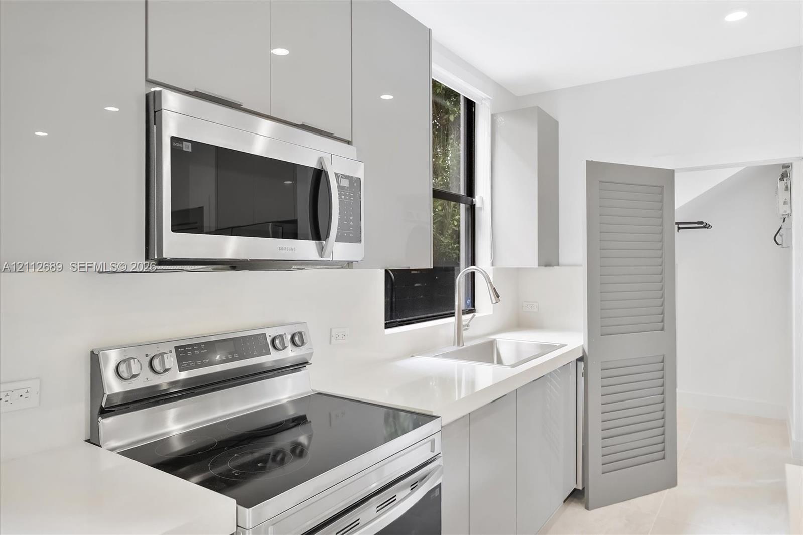 Kitchen featuring flat-panel gray cabinetry, stainless steel appliances, white solid-surface countertops, an undermount sink with a gooseneck faucet, and a louvered interior door