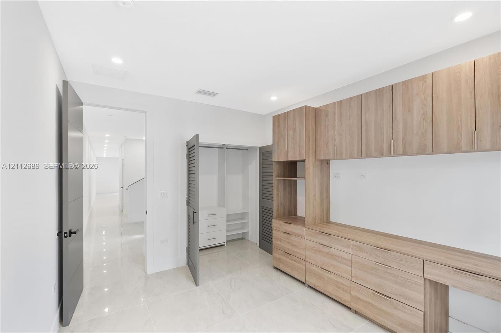 Custom wood-finish built-in cabinetry, integrated desk workspace, recessed lighting, polished tile flooring, and louvered-door closet