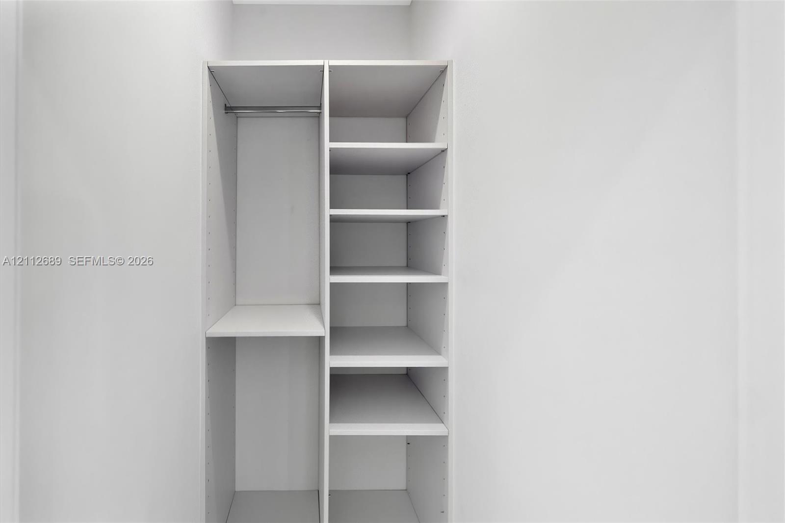 Built-in closet system featuring white shelving, adjustable rack pinholes, and a metal hanging rod