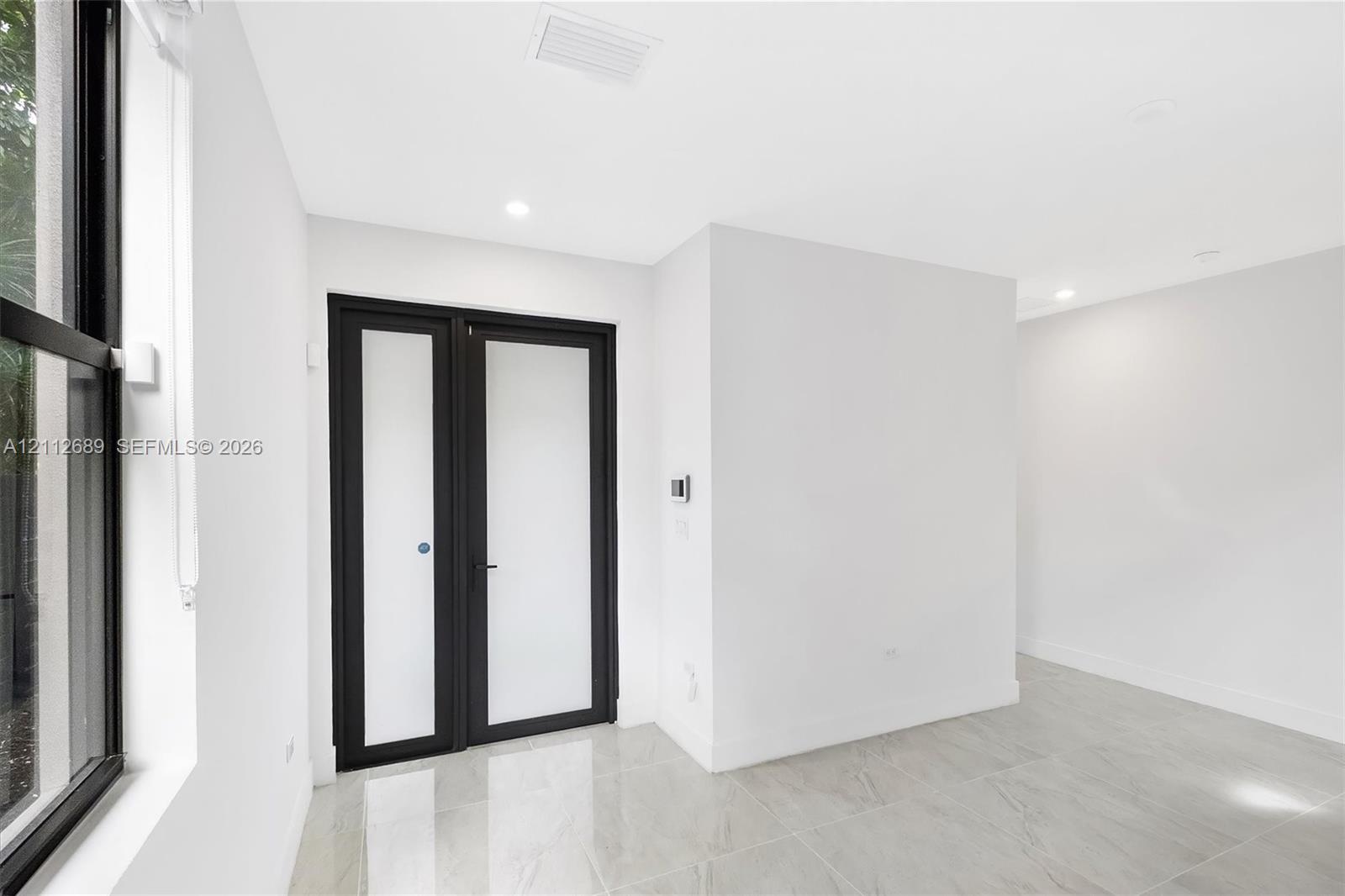 Neutral-toned tile flooring, recessed ceiling lighting, and double doors featuring frosted glass panels with matte black frames