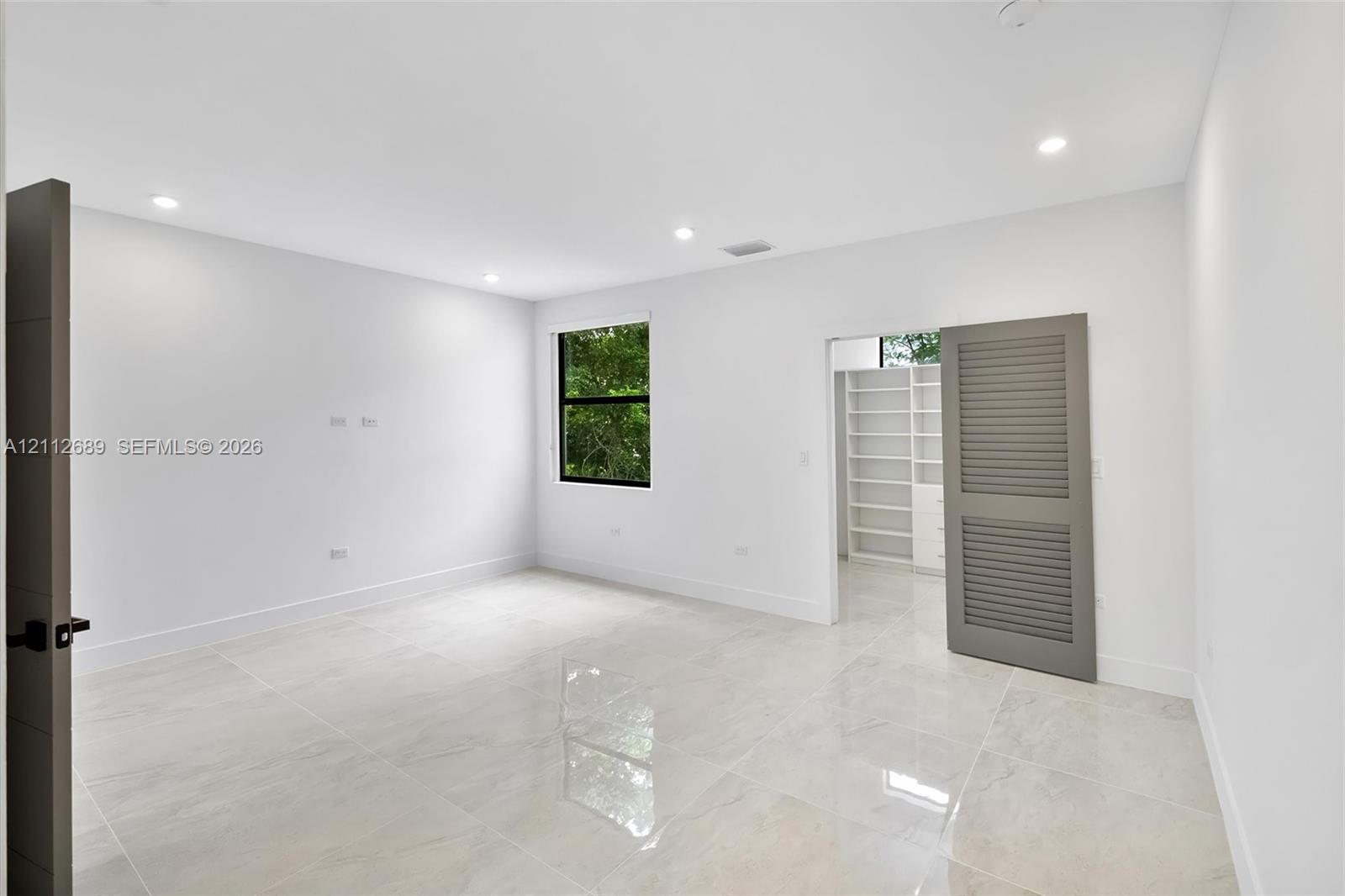 Neutral-toned polished tile flooring, recessed ceiling lighting, louvered panel door, and built-in shelving unit