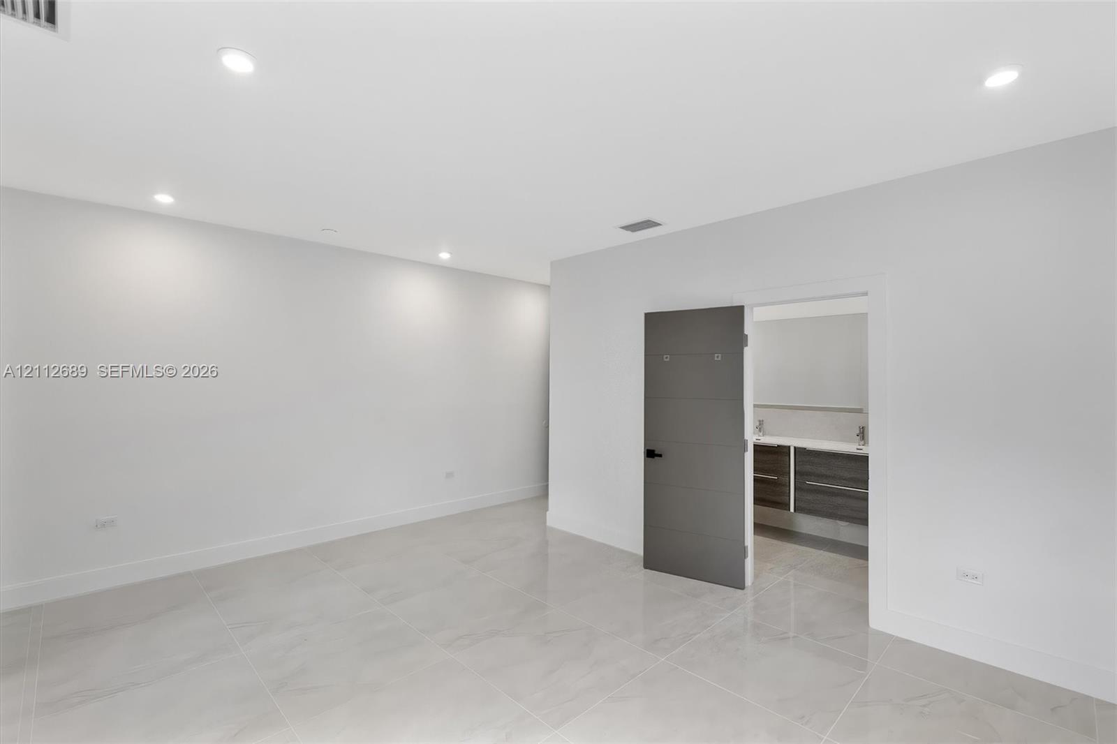 Neutral-toned large-format tile flooring, recessed ceiling lighting, and a modern slab-style interior door featuring horizontal accent grooves and matte black hardware