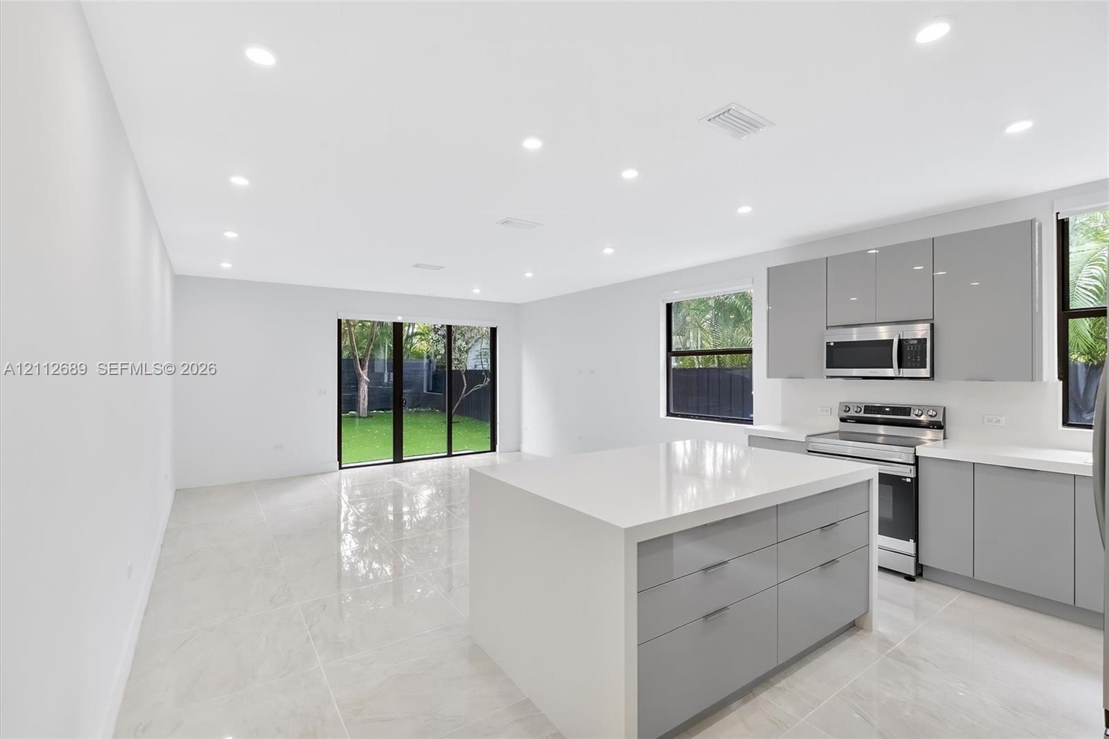 Open-concept kitchen featuring high-gloss cabinetry, a central island with a solid surface countertop, stainless steel appliances, recessed lighting, and large-format tile flooring