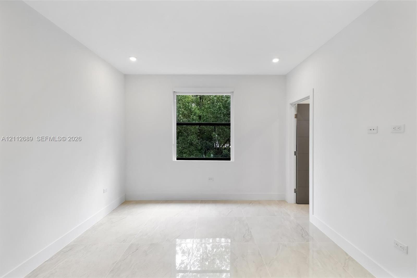 Interior space featuring large-format polished tile flooring, recessed lighting, neutral wall paint, and a single window with exterior greenery