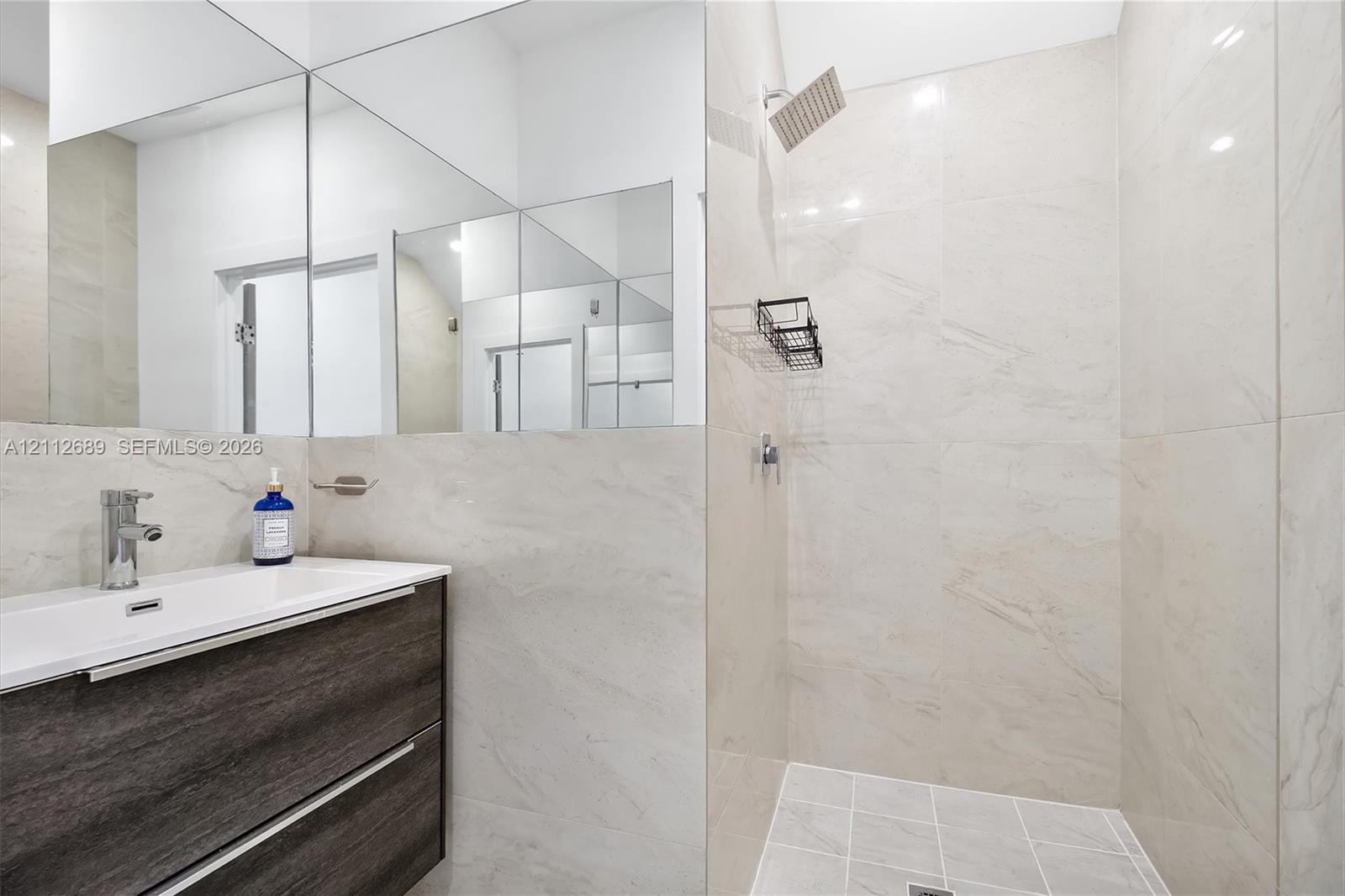 Modern floating vanity with a dark wood-finish exterior, integrated rectangular sink, wall-spanning mirror, and a walk-in shower featuring large-format wall tile and a rainfall showerhead