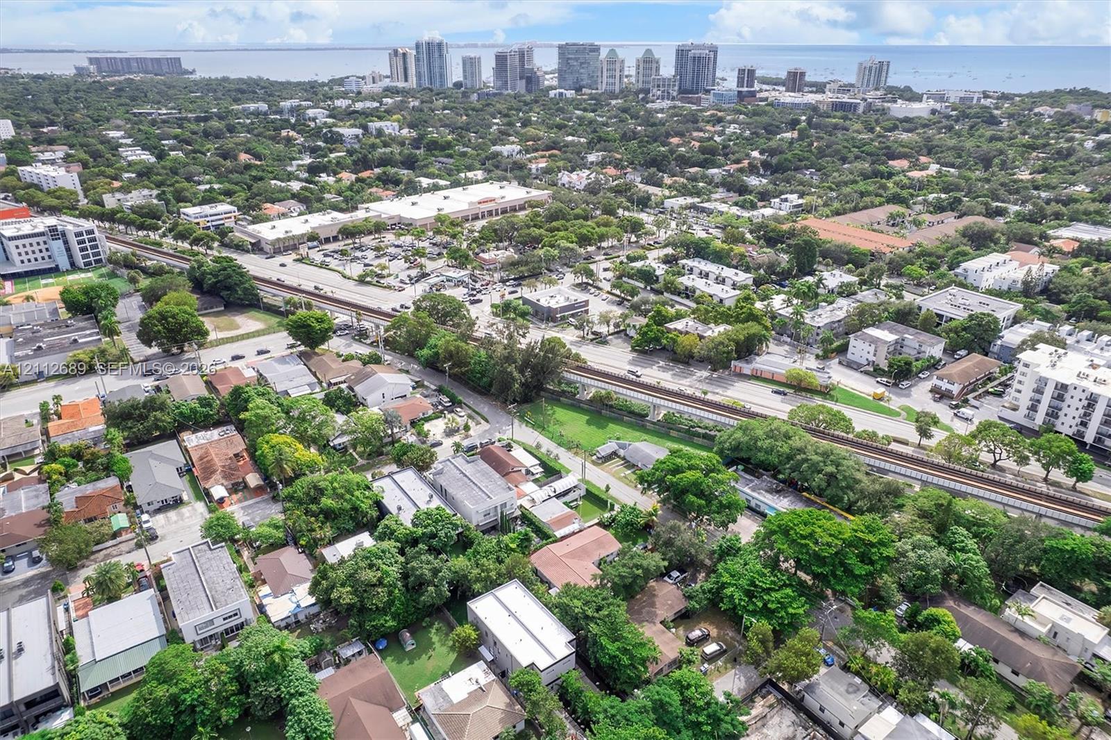 Aerial perspective of a suburban environment featuring mature tree canopy, proximity to commercial infrastructure, and a coastal skyline backdrop