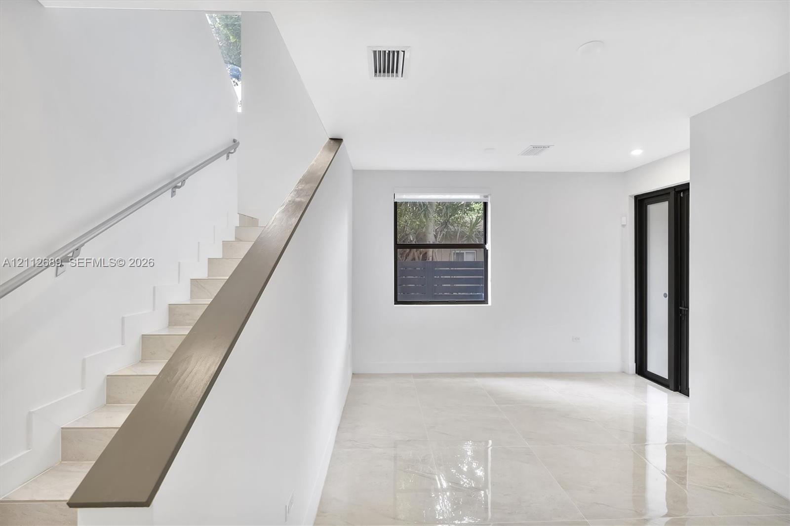 Interior space featuring polished tile flooring, a staircase with a minimalist metal handrail, a dark-finished accent banister, and a door with black framing
