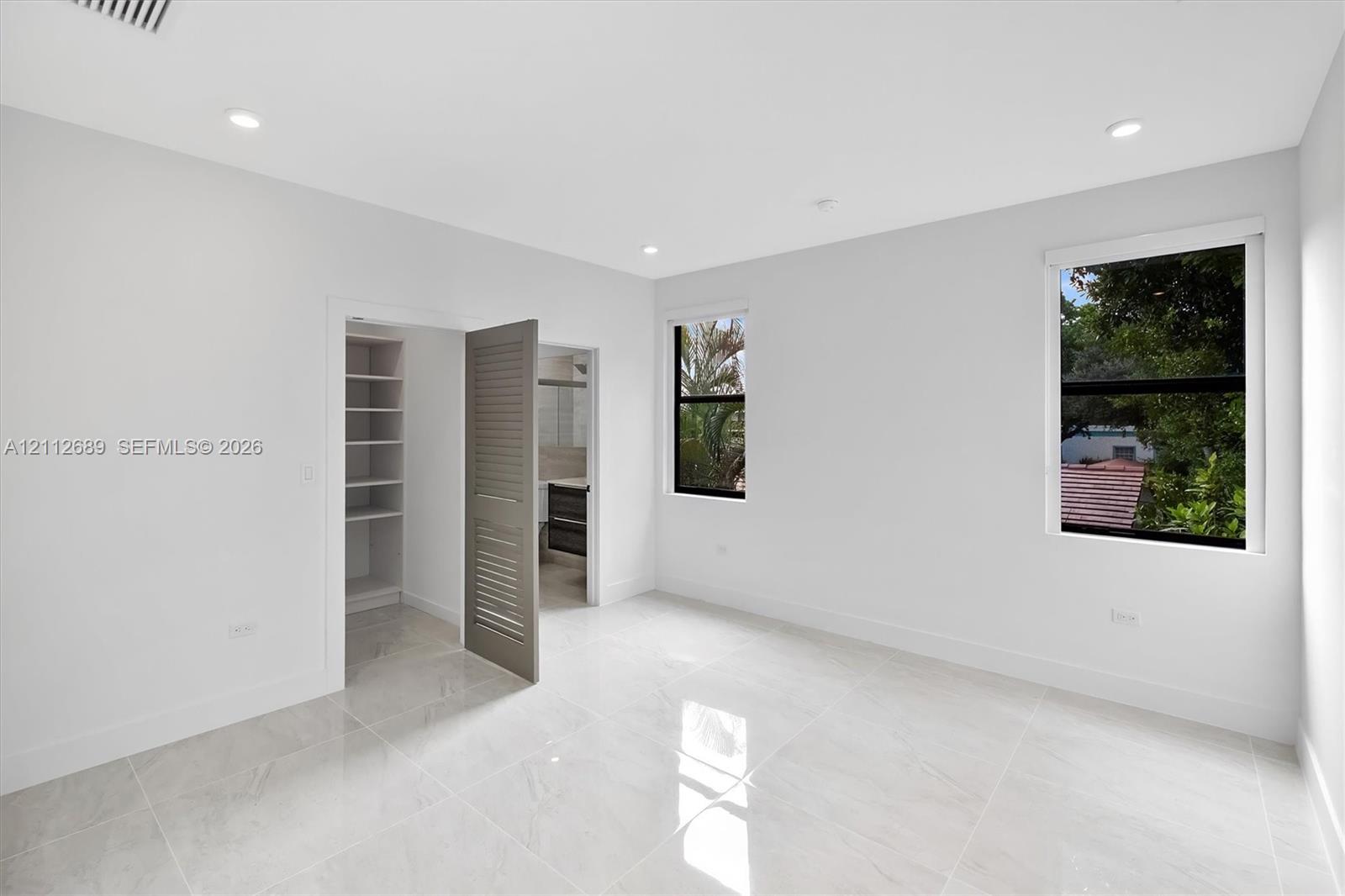 Interior space featuring polished porcelain tile flooring, recessed lighting, double-pane windows with black frames, and a walk-in closet with custom built-in shelving