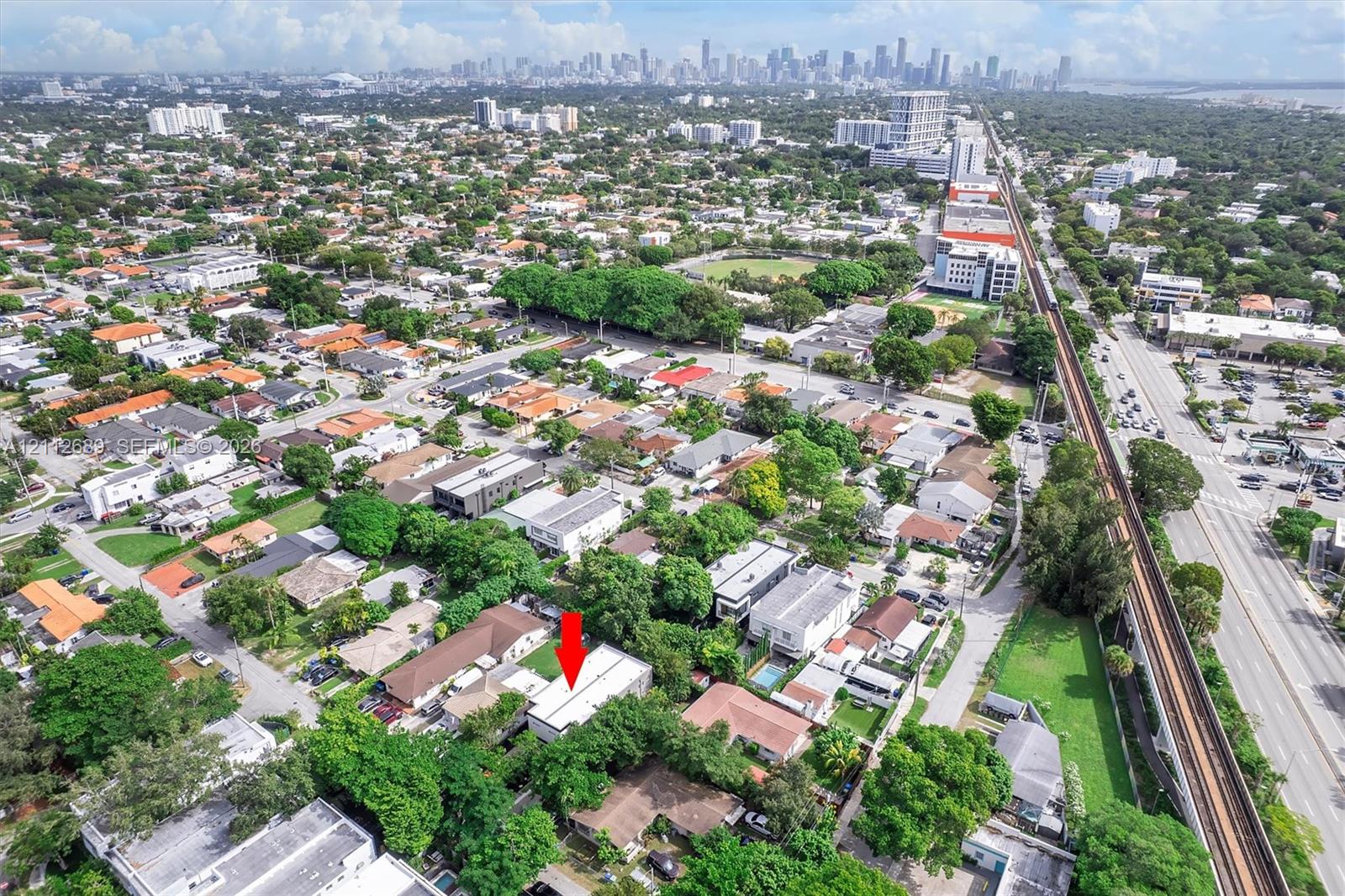 Aerial perspective featuring urban proximity, mature tree canopy, and a flat-roof residential structure