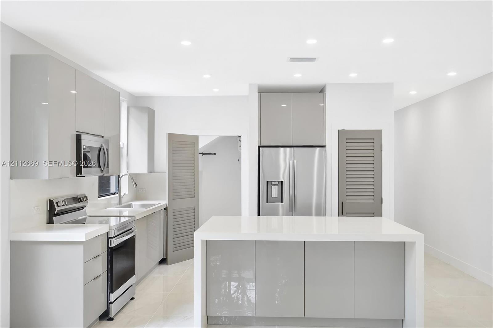 Contemporary kitchen featuring high-gloss cabinetry, a central island with a solid-surface countertop, stainless steel appliances, recessed ceiling lighting, and large-format tile flooring