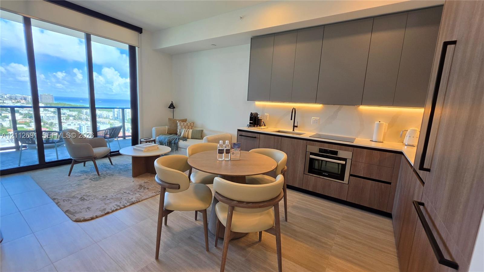Contemporary kitchen featuring flat-panel two-tone cabinetry, stone-finish countertops with integrated backsplash, built-in wall oven and cooktop, wood-finish flooring, and floor-to-ceiling windows