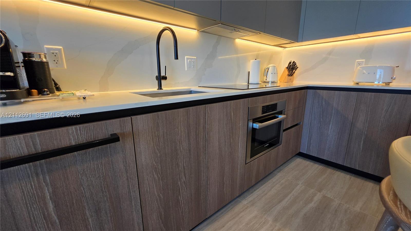 Kitchen featuring flat-panel wood-grain cabinetry, quartz countertops, integrated under-cabinet lighting, a matte black gooseneck faucet, and a stainless steel built-in wall oven