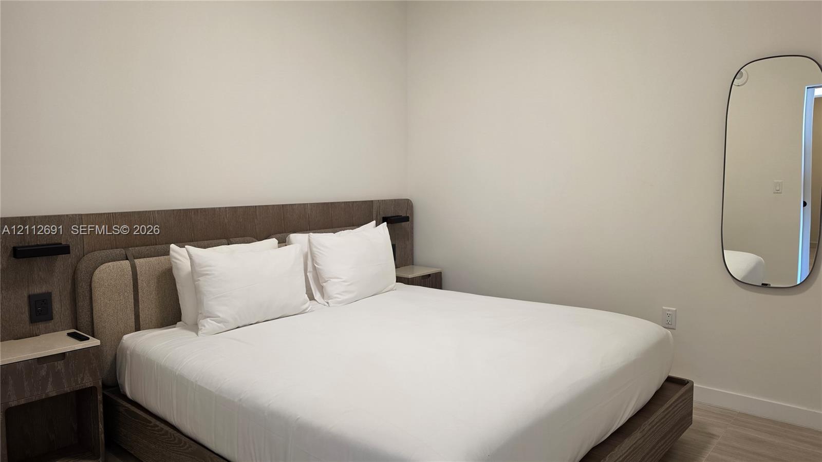 Integrated wood-finish headboard with built-in side tables, low-profile bed platform, and oval wall-mounted mirror