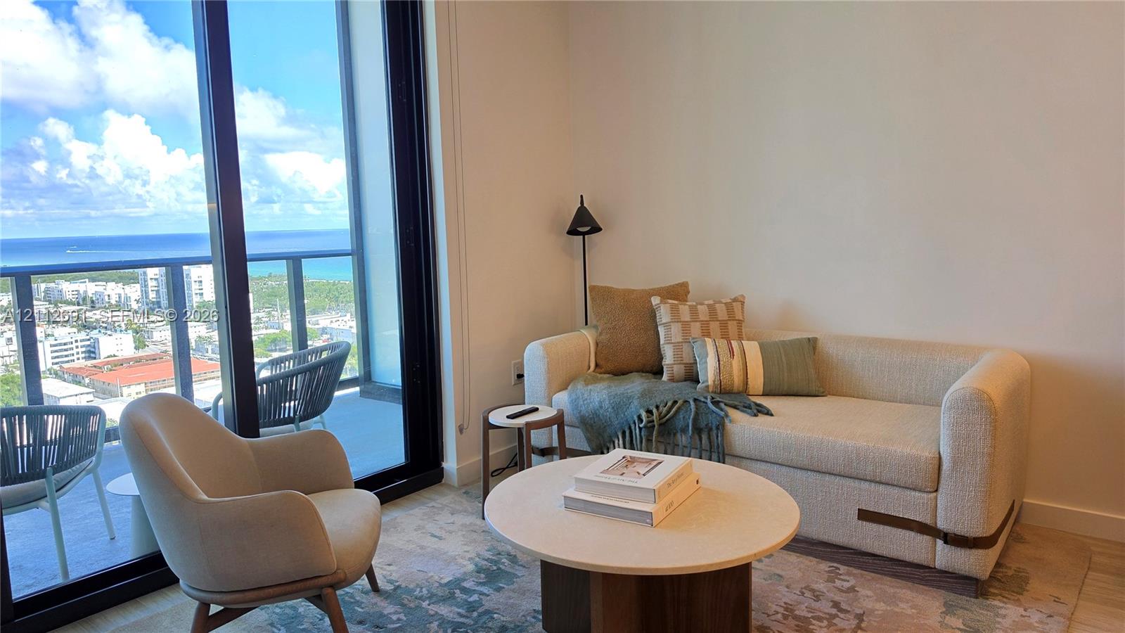 Floor-to-ceiling glass sliding doors, covered balcony with metal railing, and light-toned flooring