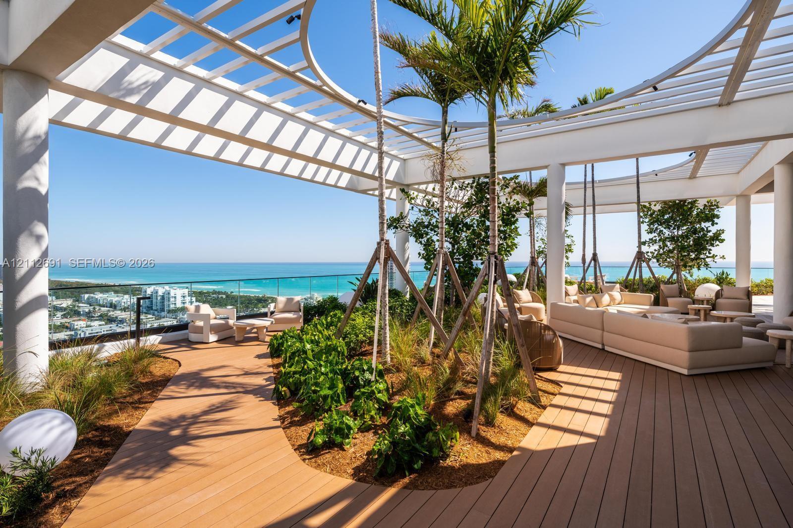Expansive terrace featuring a circular architectural pergola, wood-finish decking, integrated landscape planters with palm trees, and a glass panel perimeter railing