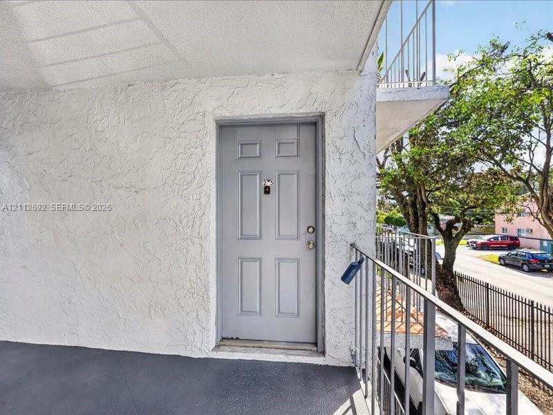 Exterior entry featuring a textured stucco facade, a paneled door with hardware, and a metal railed walkway