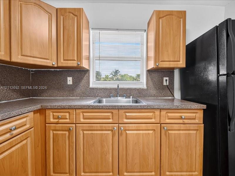 Kitchen featuring wood-finish cabinetry, speckled laminate countertops, a stainless steel sink with a dual-handle faucet, and an integrated black refrigerator