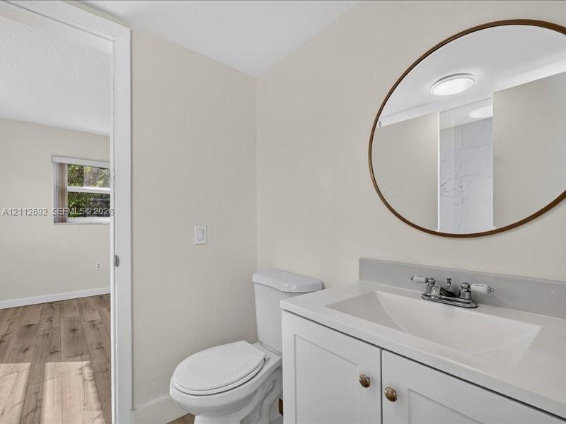 White vanity with a rectangular integrated sink, neutral stone-finish backsplash, oval mirror with a metallic frame, and a dual-handle faucet