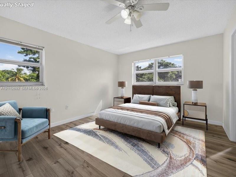 Wood-finish flooring, dual windows with exterior foliage, and a ceiling-mounted light fixture with fan