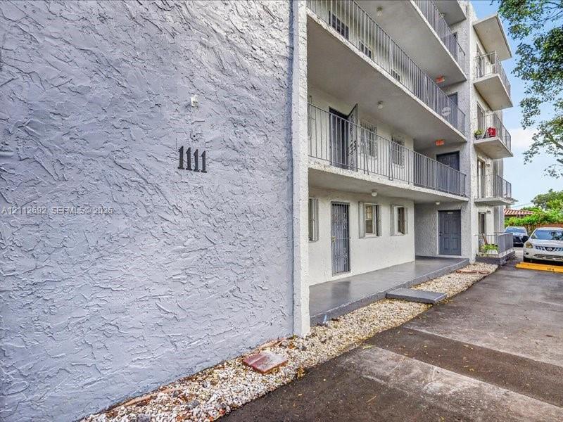 Multi-level building exterior featuring textured stucco siding, stacked balconies with metal railings, and a gravel border