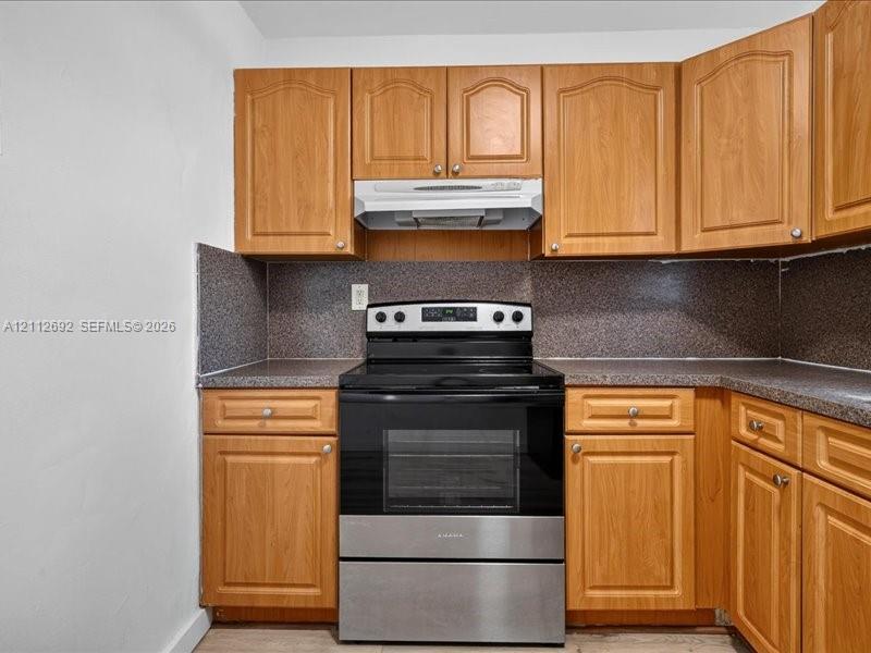 Kitchen featuring arched-panel wood cabinetry, stone-composite countertops, and an integrated stainless-steel range with a matching overhead hood