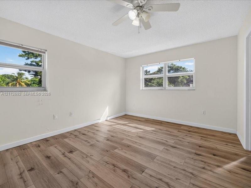 Neutral-toned interior space featuring wood-finish flooring, dual windows, and a ceiling-mounted light fixture with fan