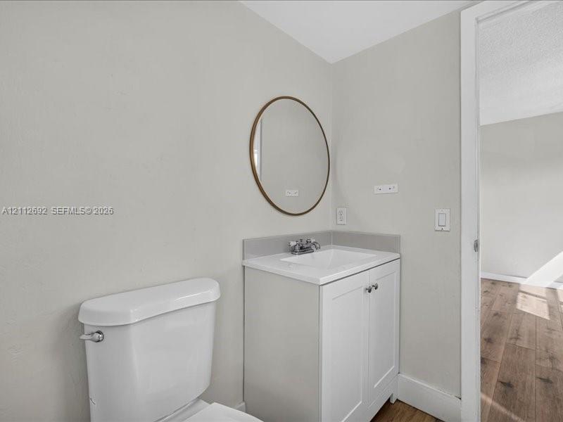 White vanity with integrated basin, chrome-finish dual-handle faucet, oval-shaped wall-mounted mirror with bronze-toned frame, and white porcelain toilet