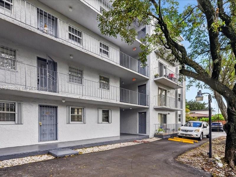Multi-story structure with a textured stucco facade, tiered exterior balcony walkways, metal railings, and dedicated asphalt parking