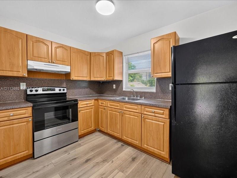 Kitchen featuring wood cabinetry, stone-composite countertops, stainless steel range with overhead hood, and wood-finish flooring