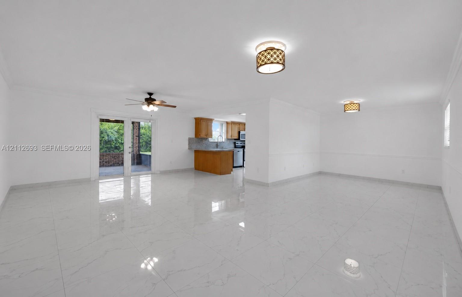 Open-concept interior featuring large-format tile flooring, double glass doors, ceiling fan, and decorative flush-mount lighting fixtures
