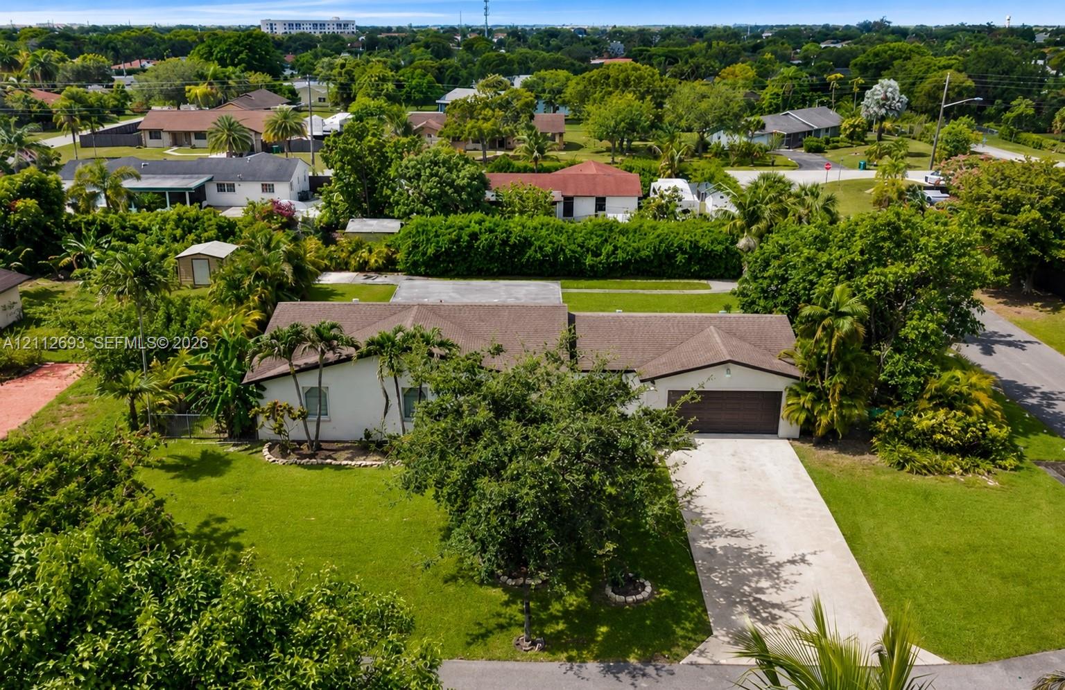 Single-story residence featuring a shingled roof, stucco exterior, attached two-car garage, concrete driveway, and expansive lot with mature landscaping