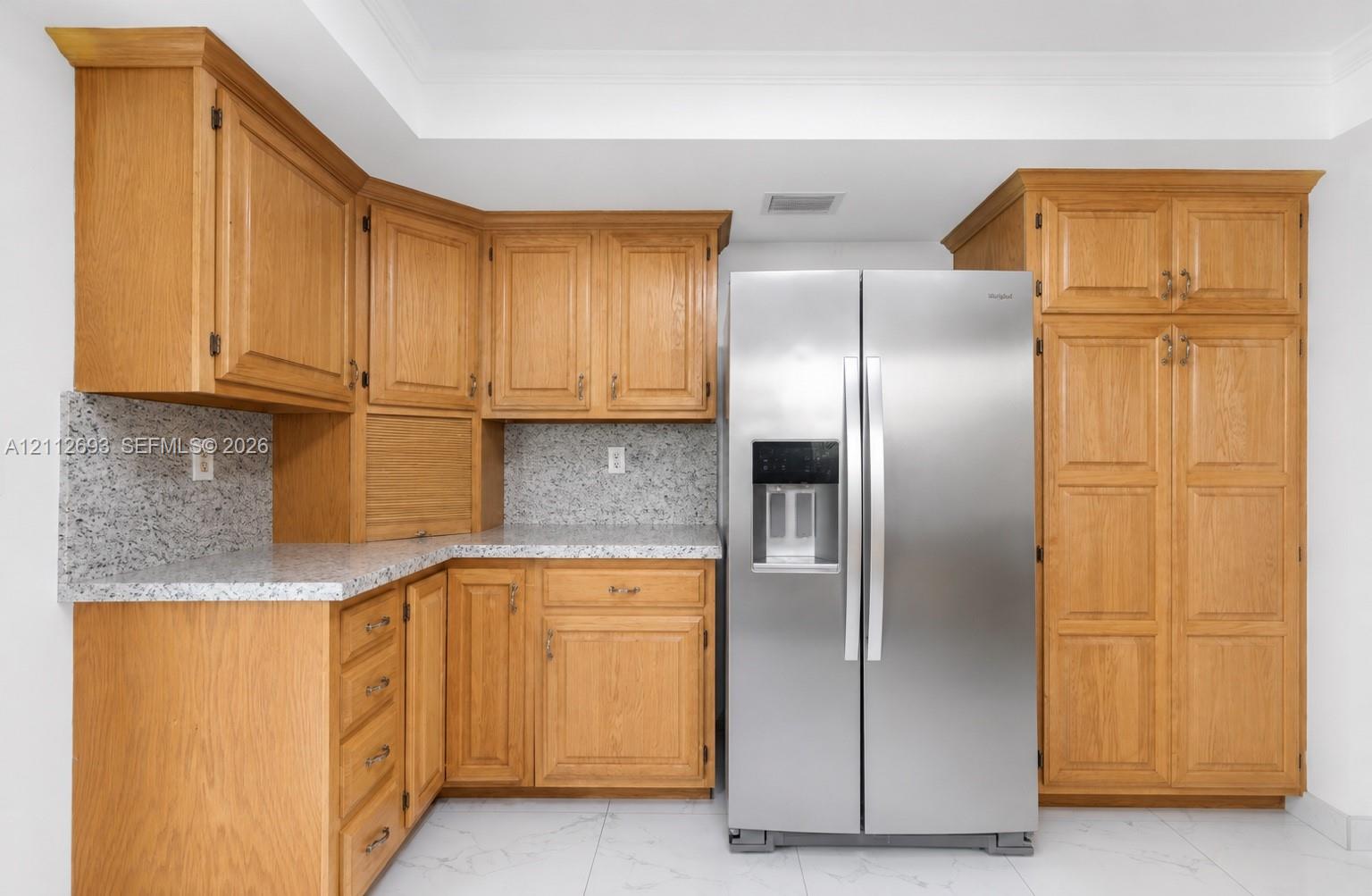 Kitchen featuring natural wood cabinetry, light-toned speckled stone countertops, and a side-by-side stainless steel refrigerator with an integrated water and ice dispenser