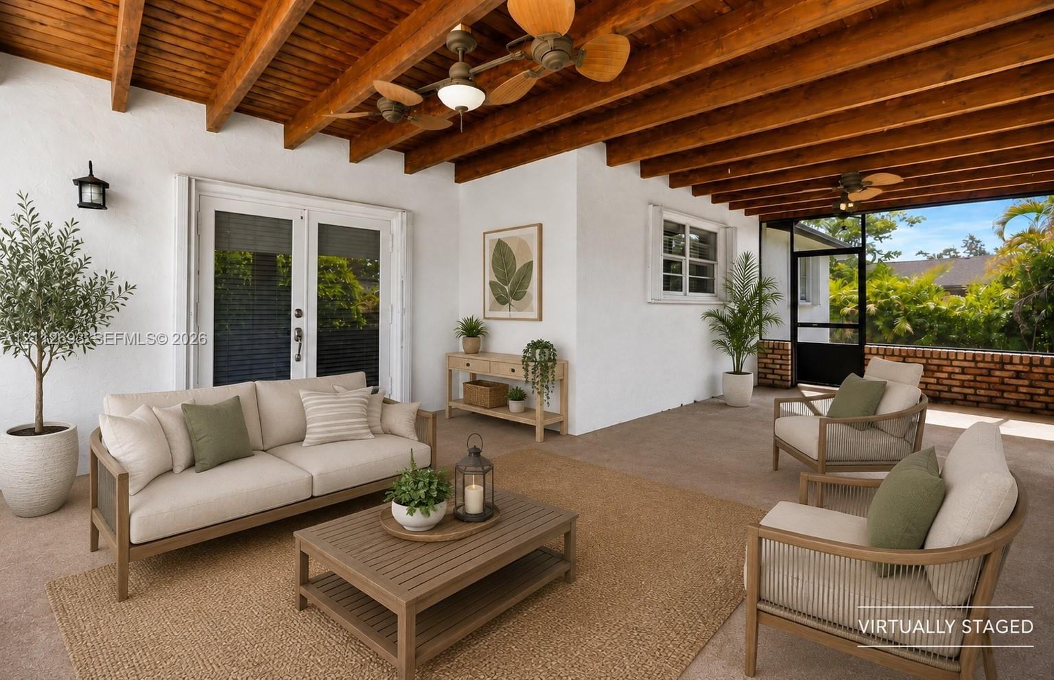 Covered patio featuring exposed wood beam ceilings, double French doors, dual ceiling fans, wall-mounted light fixtures, and a masonry brick perimeter wall