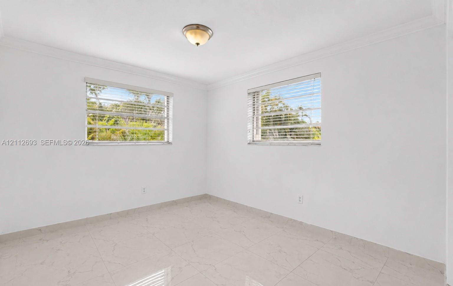 Neutral-toned tile flooring, white walls, crown molding, two windows with horizontal blinds, and a semi-flush mount ceiling fixture