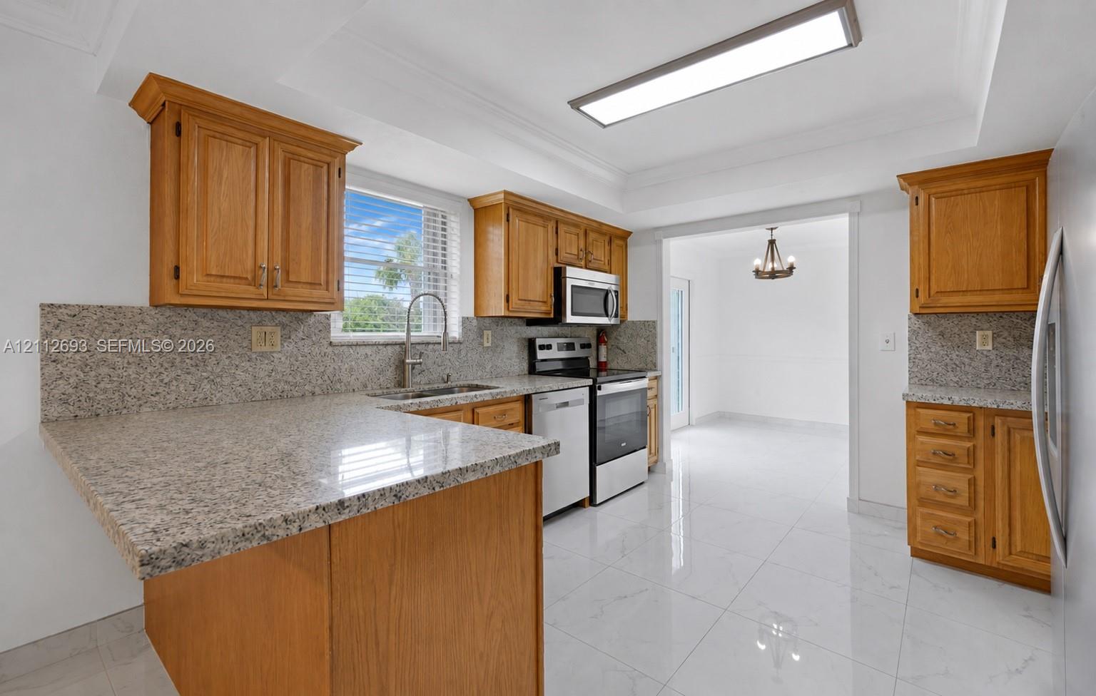 Kitchen featuring wood cabinetry, stone countertops, stone backsplash, stainless steel appliances, and large-format tile flooring