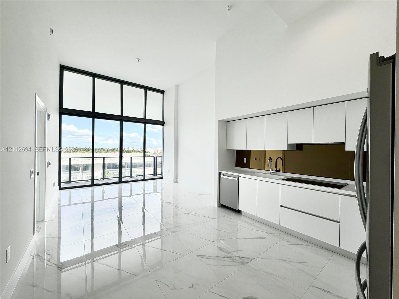 Open-concept interior featuring floor-to-ceiling windows, high ceilings, large-format tile flooring, white cabinetry, and a mirrored backsplash